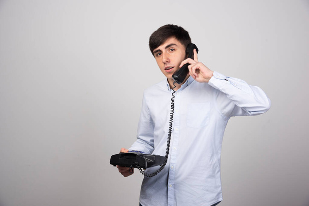 Jeune homme parlant avec quelqu'un via téléphone fixe sur fond gris. Photo de haute qualité - Photo, image