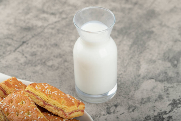 Kokonaiset keksejä seesaminsiemeniä ja lasi kannu maitoa sijoitetaan kivi pöydälle. Laadukas kuva - Valokuva, kuva