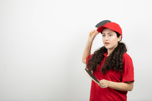 Brunetka w czerwonym mundurze bawiąca się rakietami do tenisa stołowego. Wysokiej jakości zdjęcie - Zdjęcie, obraz
