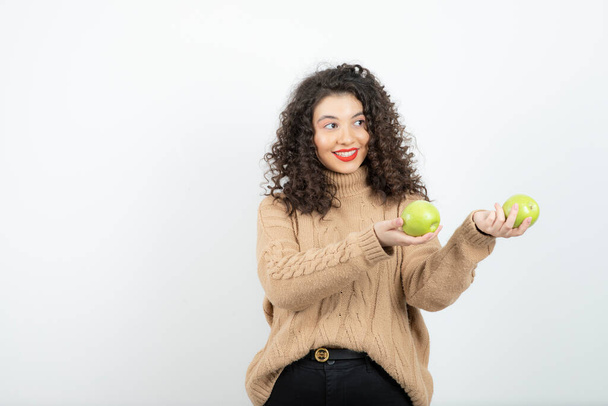 Imagen de mujer rizada con lápiz labial rojo con manzanas verdes de pie. Foto de alta calidad - Foto, imagen