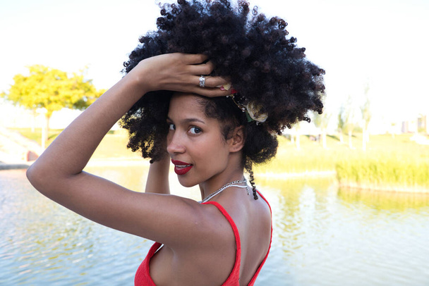 beautiful young afro american woman doing different poses and gestures on camera. She wears in her hair a crown of pink flowers and a red top. Lifestyle concept - Zdjęcie, obraz