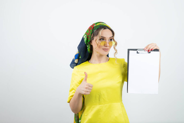 Photo of cute woman in headkerchief with clipboard showing thumb up. High quality photo - Photo, Image