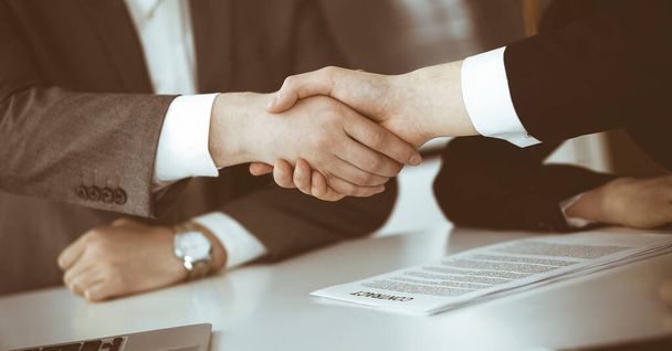 Unknown businessman shaking hands with his colleague or partner above the glass desk in modern office, close-up. Business people group at meeting - Foto, afbeelding