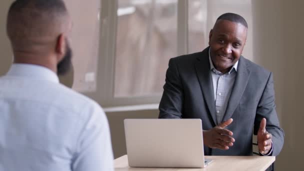 Dojrzałe stary Afryki szef szef amerykański lider biznesu człowiek agent bank manager wyjaśnić doradza rozmowy siedzi przy stole z laptopem komunikuje się z nierozpoznawalny afro facet etniczny czarny klient pracownik - Materiał filmowy, wideo