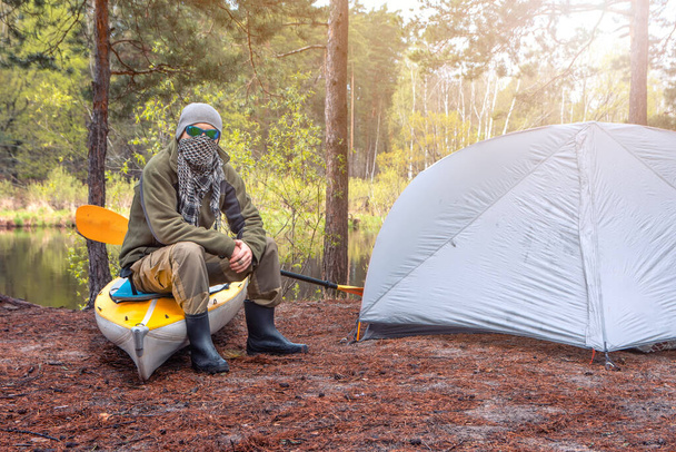 duro sedersi vicino alla tenda e il suo kayak nella foresta sulla riva del fiume. concetto tenda da campeggio all'aperto - Foto, immagini