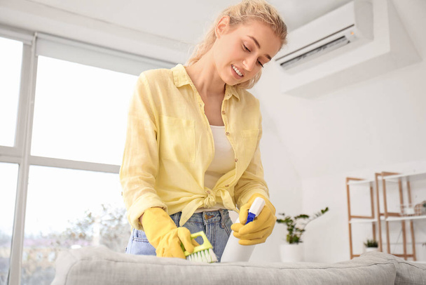 Young woman cleaning sofa in her flat - Photo, Image