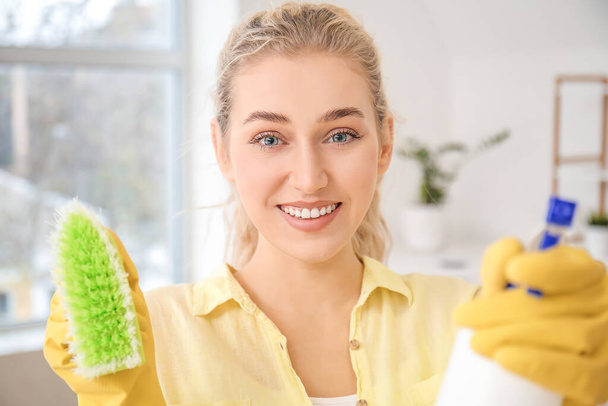 Νεαρή γυναίκα με απορρυπαντικό και βούρτσα καθαρισμού στο σπίτι - Φωτογραφία, εικόνα