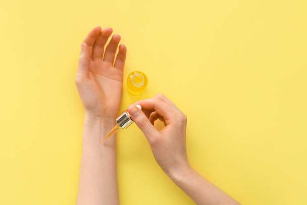 Woman applying essential oil onto her hand against color background - Photo, Image