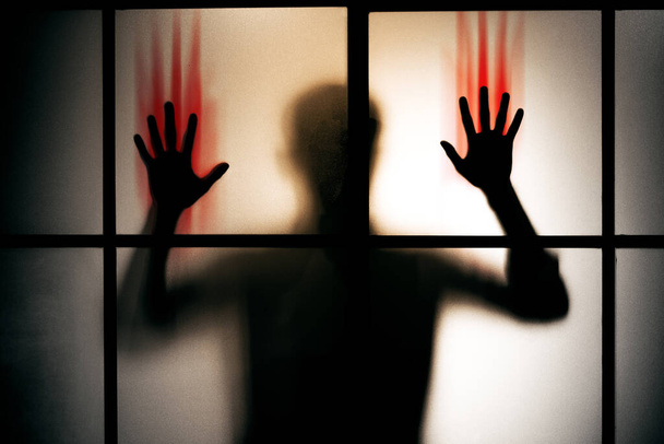σιλουέτα φοβισμένος άνθρωπος με κόκκινο αιματηρό χέρι σταθεί πίσω από γυάλινη πόρτα, φόντο τρόμου - Φωτογραφία, εικόνα