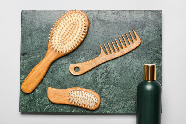 Board with hair brushes, comb and bottle of cosmetic product on grey background - Fotoğraf, Görsel