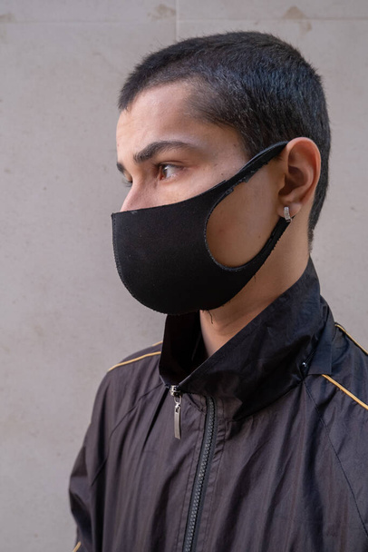 Молодий чоловік в масці для обличчя дивиться в бік під час пандемії
. - Фото, зображення