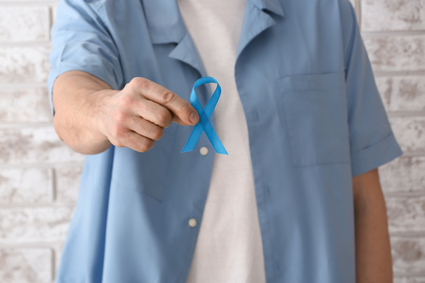 Άντρας με μπλε κορδέλα κοντά σε ανοιχτό τοίχο από τούβλα, κοντά. Έννοια του καρκίνου του προστάτη - Φωτογραφία, εικόνα