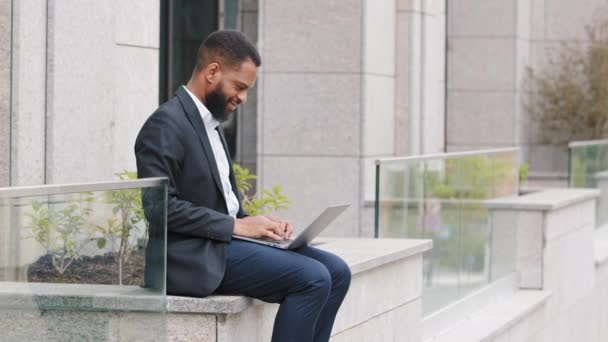 Der bärtige junge Mann mit dem Laptop sitzt auf Knien im Freien und hat ein technisches Gerät dabei. Afrikaner tippt auf Computer, surft im Internet Studie kommunizieren Online-Surfen im Web - Filmmaterial, Video