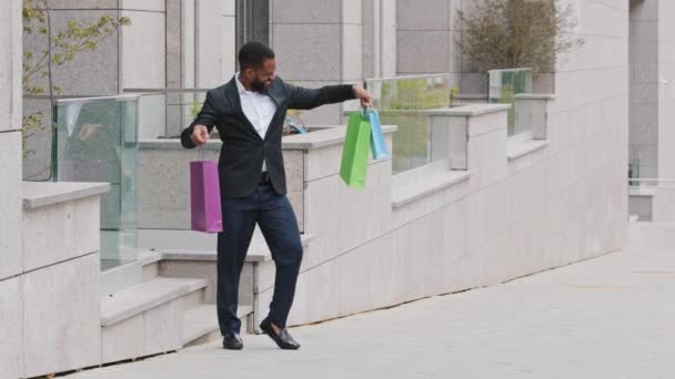Millennial nuori aikuinen musta mies opiskelija, henkilökohtainen avustaja kävely ulos ostoskeskuksen putiikki myymälä paperipussit. Pomo osti lahjoja työntekijöille, uusia vaatteita, hyviä asioita, onnellisia onnistuneita ostoksia - Materiaali, video
