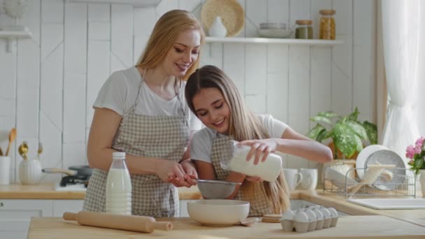 Meisje tiener kind dochter helper helpt moeder om samen te koken dragen schorten zeven tarwemeel door een ijzeren zeef ingrediënten toe te voegen voor zelfgemaakte taart, moeder leert kind om taart te maken in de keuken thuis - Video