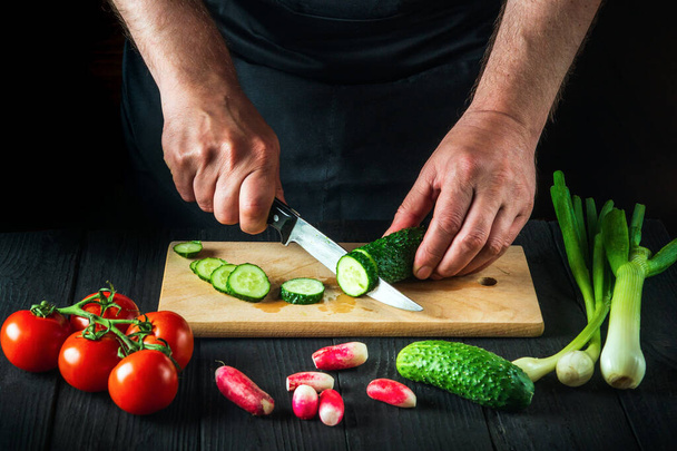 Profi-Koch schneidet auf einem Schneidebrett in der Restaurantküche eine grüne Gurke für Salat. Gemüseernährung oder Snack-Idee. - Foto, Bild