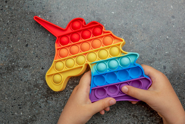 Поп-это игрушка, радуга цвета, в виде единорога. Красочная, разноцветная, сенсорная, антистрессовая игрушка в руках у детей - Фото, изображение