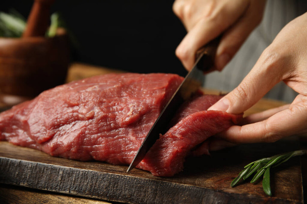 Woman cutting fresh raw meat at wooden table, closeup - Foto, immagini