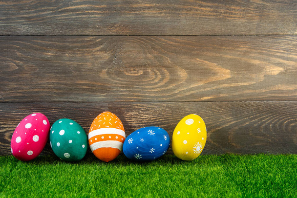 Happy Easter background. Easter eggs on green grass on wooden background. Festive Easter banner with painted colorfull eggs. Copy space - Фото, зображення