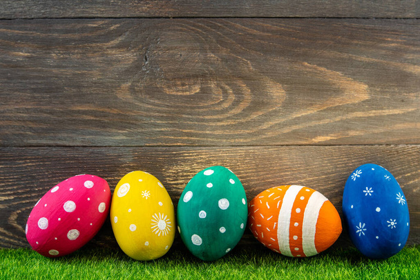 Feliz Pascua. Huevos de Pascua sobre hierba verde sobre fondo de madera. Banner festivo de Pascua con huevos coloridos pintados. Copiar espacio - Foto, Imagen