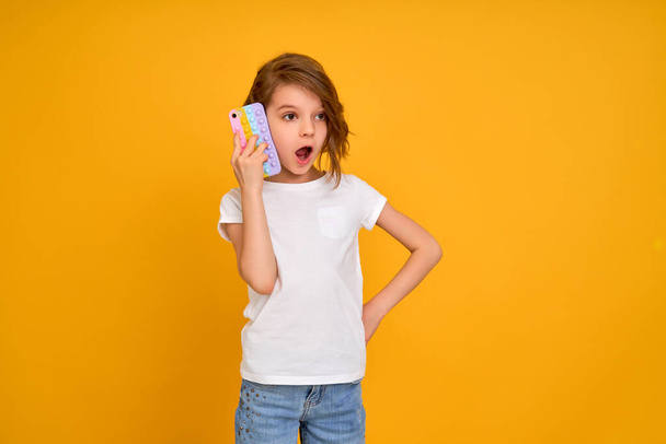 Surprized little girl holding telephone with open mouth isolated over yellow color background - Foto, Bild