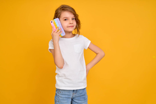 Holčička drží telefon izolované přes žlutou barvu pozadí - Fotografie, Obrázek