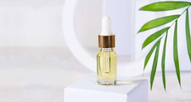 Natural cosmetics product in glass bottle with dropper, skin care beauty product - serum, lotion, herbal cosmetic on white podium with green leaf. Serum for woman facial skin on white stand. Copy space - Photo, Image