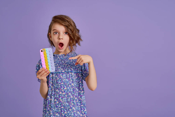 Surprized little girl holding telephone with open mouth isolated over violet color background - 写真・画像