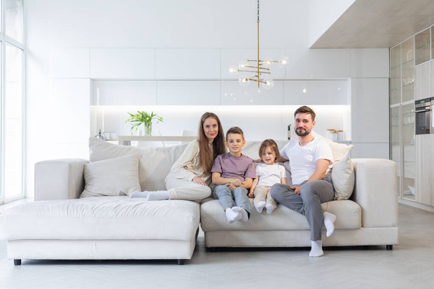 Family portrait of young parents with their two children at home, white modern desgin of living room - Valokuva, kuva