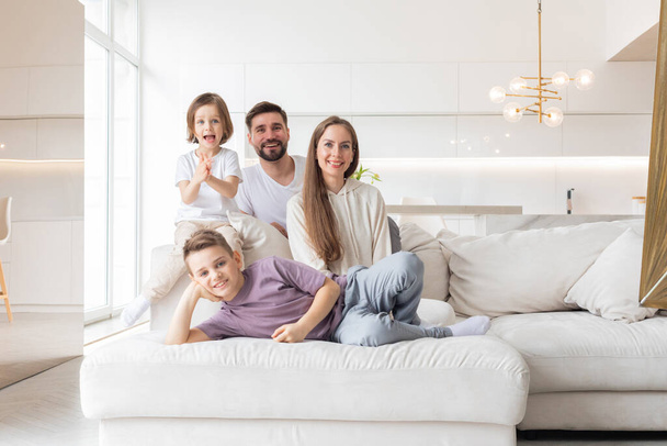 自宅で2人の子供を持つ若い両親の家族の肖像画、リビングルームの白い現代的なデザイン - 写真・画像