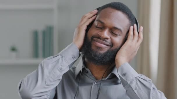 Abgelenkt von der Büroarbeit aufrichtig glücklich junge afroamerikanische Geschäftsmann biracial Manager Mitarbeiter hören Lieblings-Melodie in Kopfhörer Form Musikbibliothek Anwendung genießen hohe Klangqualität - Filmmaterial, Video
