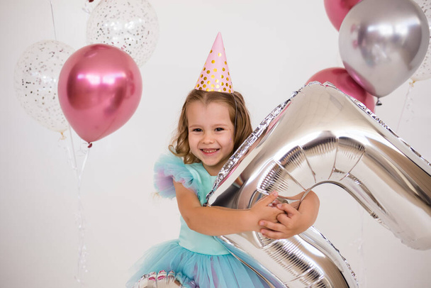 portrait of a birthday girl in a hat and a festive dress holding balloons on a white background with a place for text - Fotó, kép
