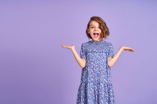 Photo of young happy surprised girl spread her hands to the sides isolated on purple color background - Фото, зображення