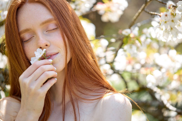 close-up portrait of beautiful woman in spring garden. female inhales the fragrance of flowering trees. - Foto, Imagem
