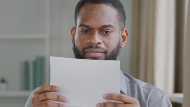 Unhappy young African guy received bad news, irritated by mistake, feeling stressed about dismissal notice. Angry black businessman opening envelope, reading banking credit loan refusal notification - Video