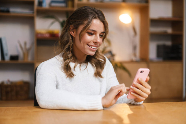 Close up de uma mulher atraente sorrindo usando telefone celular enquanto sentado no escritório moderno - Foto, Imagem