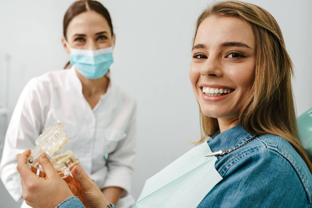 European mid happy dentist woman showing teeth imitation to her patient in dental clinic - 写真・画像