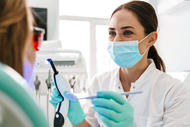 European mid pleased dentist woman in face mask working in dental clinic - Fotoğraf, Görsel