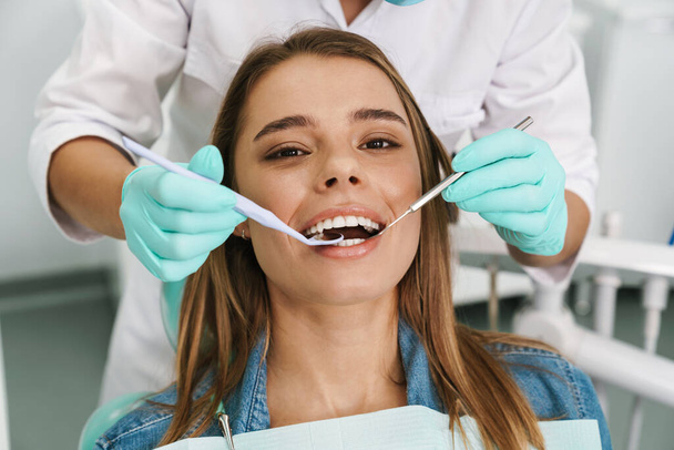 Eurooppalainen nuori nainen istuu lääketieteellisessä tuolissa hammaslääkärin korjatessa hampaitaan hammashoitolassa - Valokuva, kuva