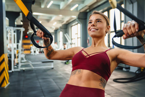 Smiling athletic sportswoman doing exercise with fitness equipment while working out in gym - Foto, Bild