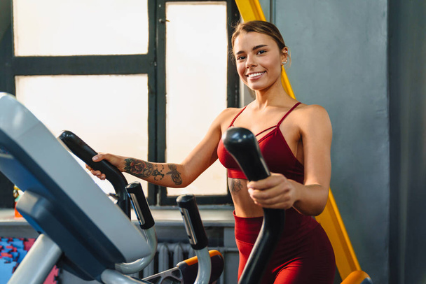 Счастливая спортсменка делает упражнения на фитнес-оборудование во время тренировки в спортзале - Фото, изображение