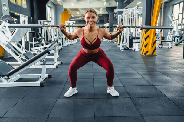 Happy athletic sportswoman doing exercise with barbell while working out in gym - Foto, Imagen