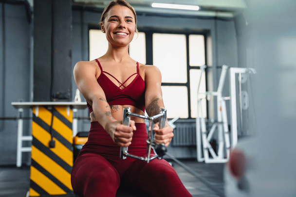 Smiling athletic sportswoman doing exercise on fitness equipment while working out in gym - Foto, afbeelding