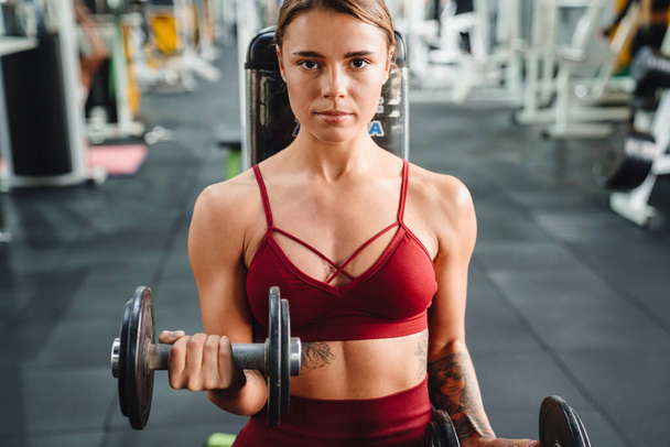 Image of strong young woman fitness coach making sport exercise for arms with dumbbells in gym - Фото, зображення