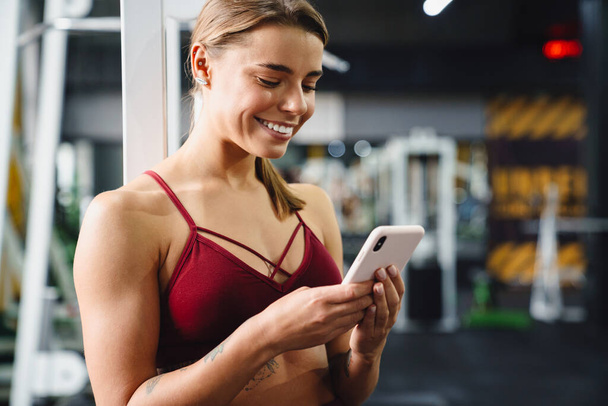 Photo of cheery positive young woman fitness coach using mobile phone in gym - Φωτογραφία, εικόνα