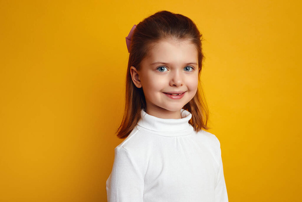 Pretty little girl in white turtleneck posing adorably on yellow background - Photo, Image