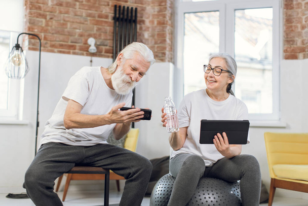 Mature couple using tablet and mobile after training at home - Photo, Image