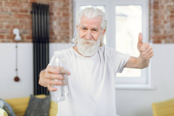Senior man showing thumb up and holding bottle of water - Foto, afbeelding