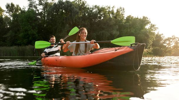 Joyful young couple having fun while kayaking in a river surrounded by the beautiful nature on a summer day - Photo, Image