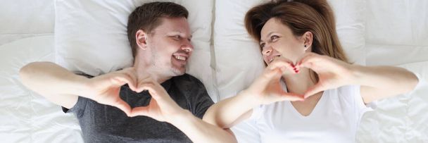 Mężczyzna i kobieta leżący w łóżku i pokazując serce z ich ręce widok z góry - Zdjęcie, obraz
